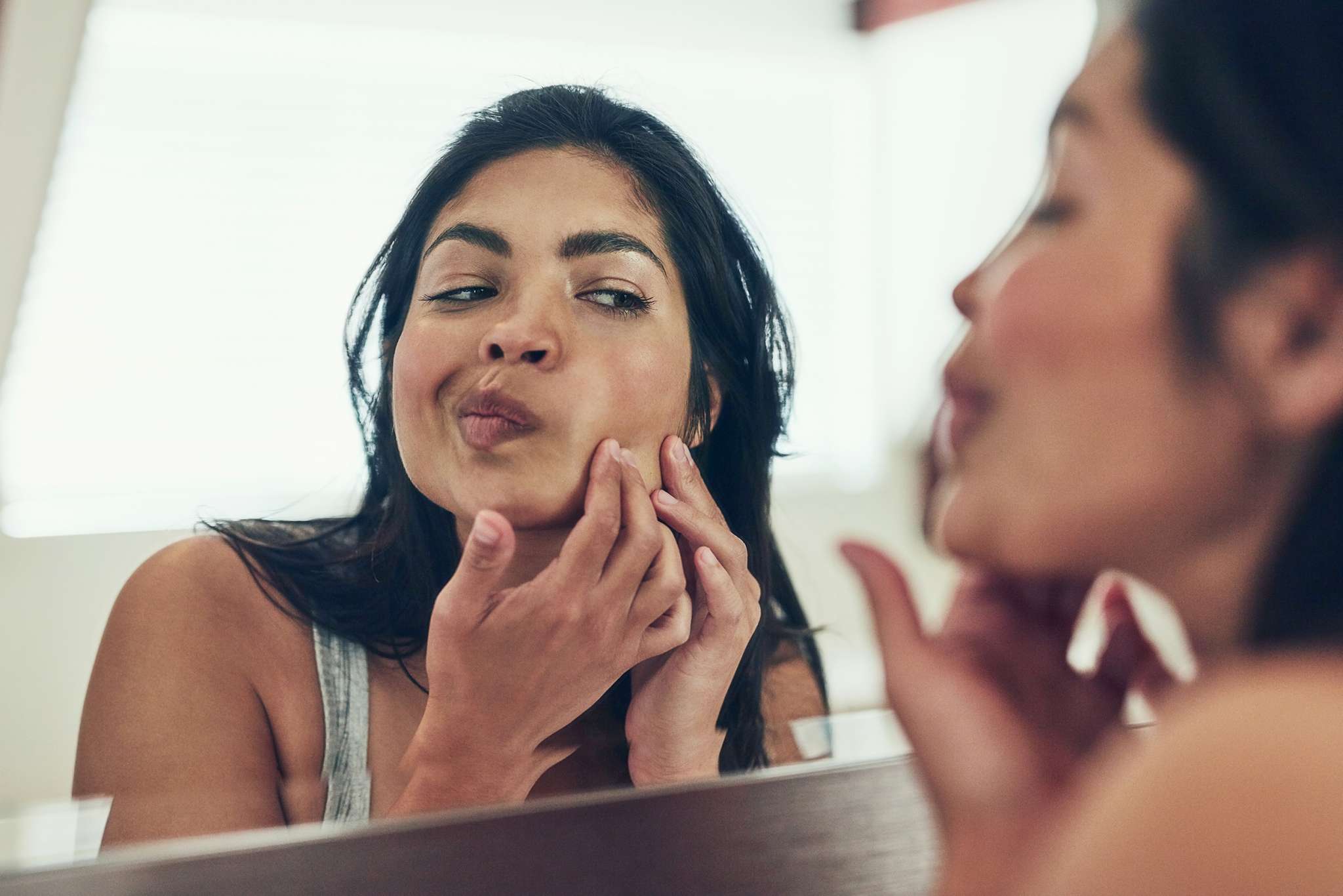 Shot of a young woman squeezing a pimple on her face at home.